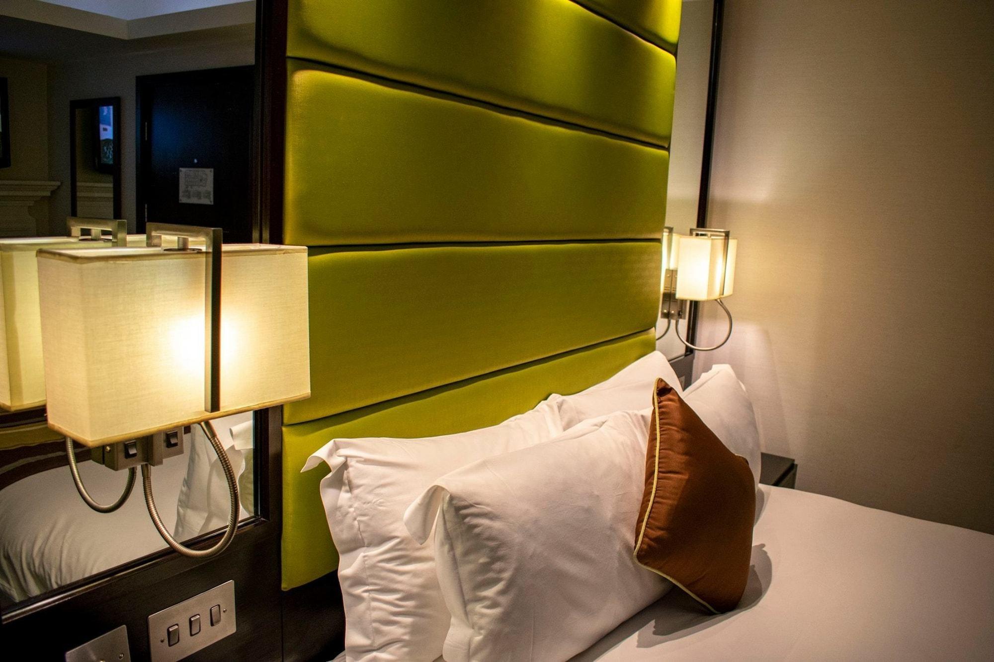 Hotel Montcalm Brewery Townhouse London Exterior foto The photo shows a modern hotel room with a stylish design. The focal point is a large bed with white pillows and a decorative brown pillow. The headboard is bright green and has a textured appearance. On either side of the bed, there are wall lamps t