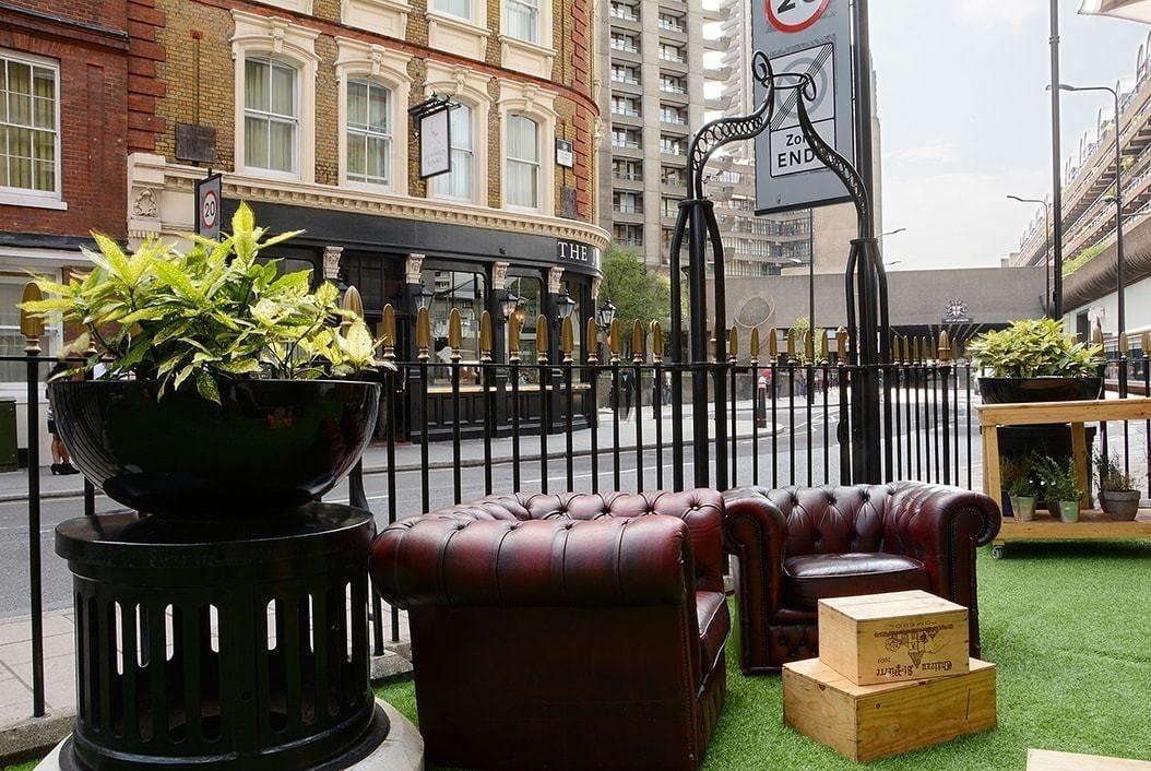 Hotel Montcalm Brewery Townhouse London Exterior foto The photo shows a street scene with a cozy outdoor seating area. There are two plush, dark leather couches arranged on green grass, creating a welcoming atmosphere. Surrounding the seating are large planters with vibrant plants. In the background, th