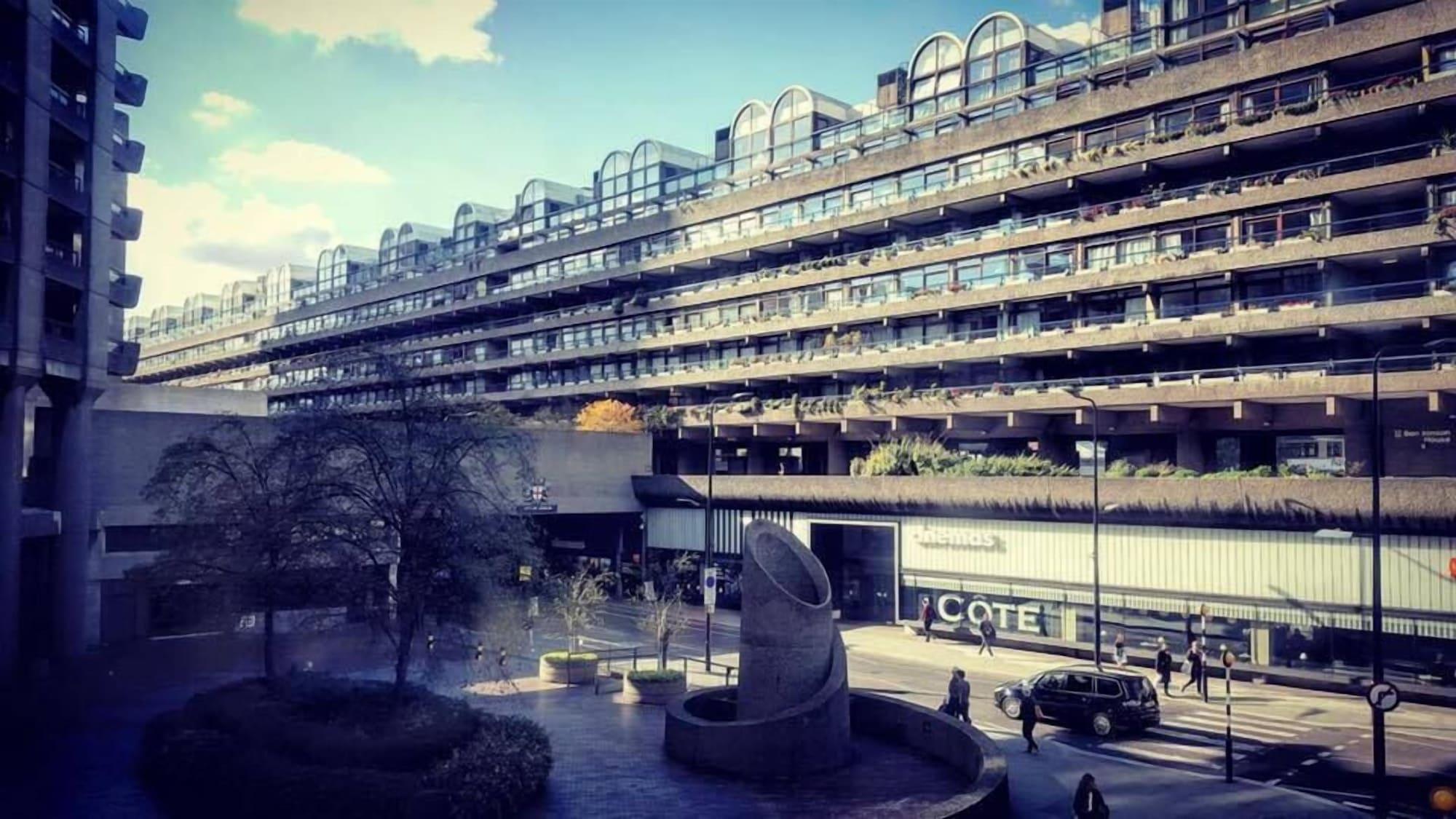 Hotel Montcalm Brewery Townhouse London Exterior foto The photo shows a modern architectural structure with multiple levels, featuring a series of large, rectangular balconies. Below this building, there is a plaza or courtyard area with a sculptural piece, which appears to be made of stone. Surrounding