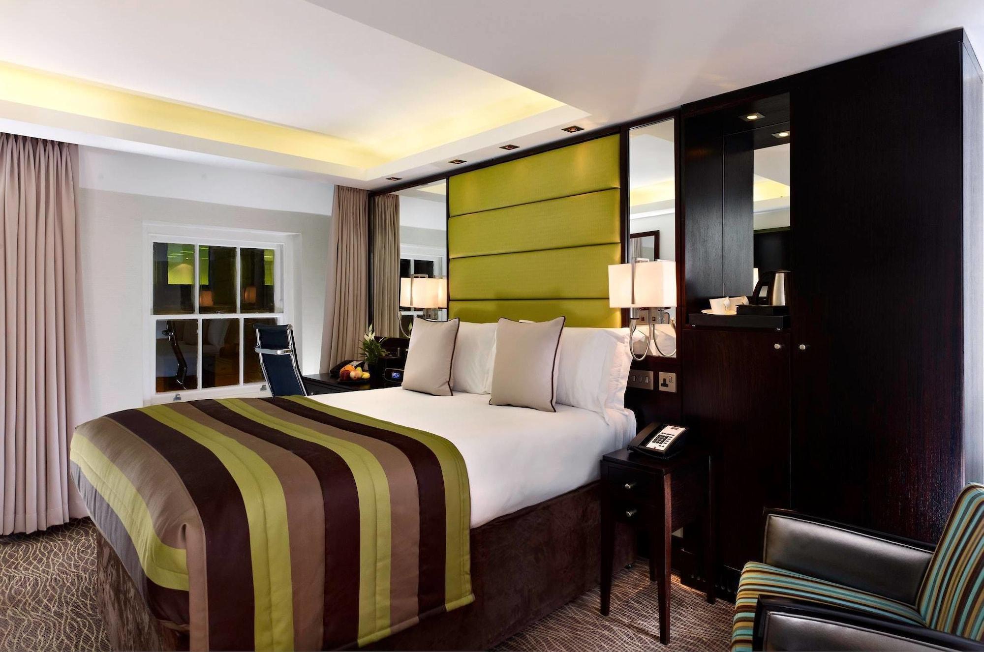 Hotel Montcalm Brewery Townhouse London Exterior foto The photo shows a modern hotel room featuring a large bed with a striped comforter in shades of green, brown, and cream. The bed is adorned with several decorative pillows. Behind the bed, there is a contemporary headboard with a green panel design. 