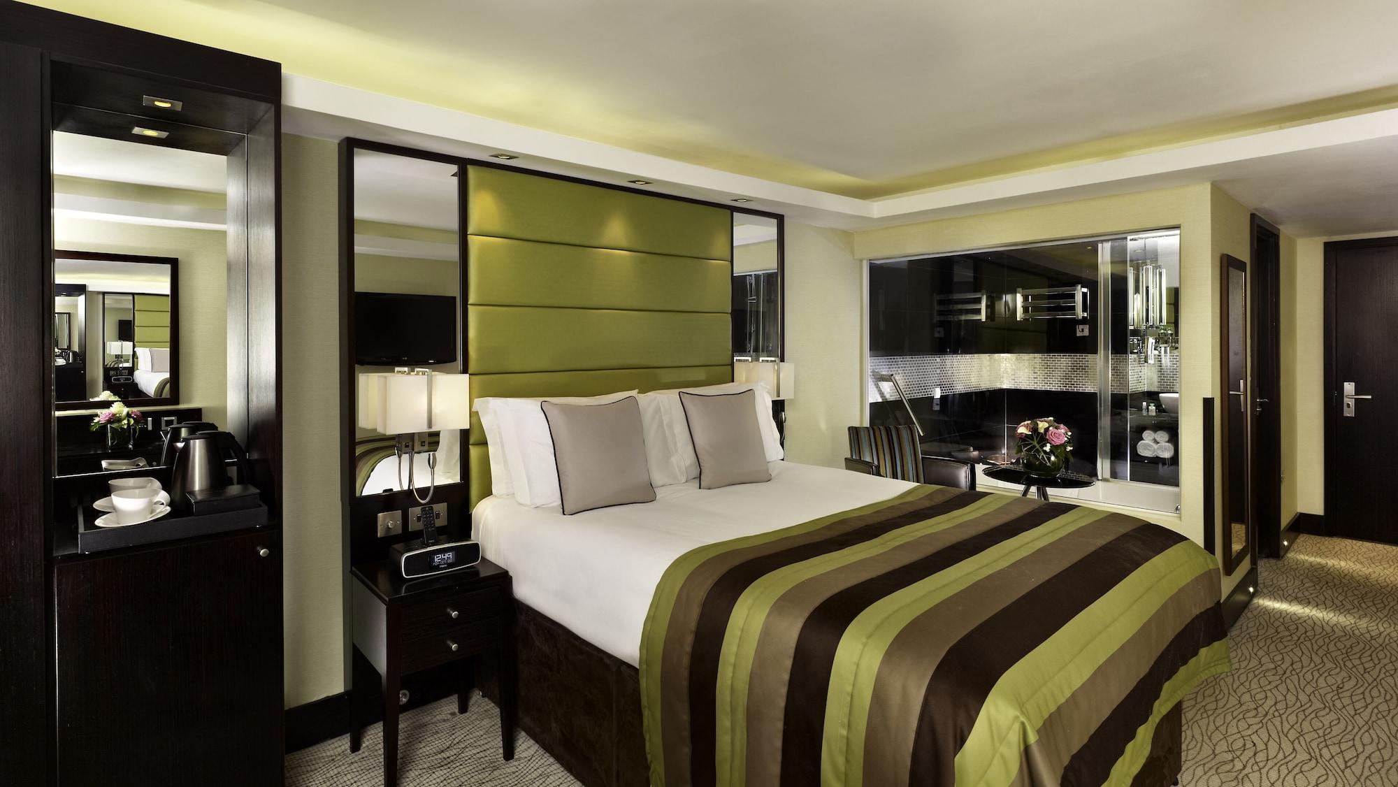Hotel Montcalm Brewery Townhouse London Exterior foto The photo shows a modern hotel room designed with a sophisticated aesthetic. It features a comfortable double bed with a striped brown and green bedspread, complemented by two light gray decorative pillows. Behind the bed is an elegant headboard sect