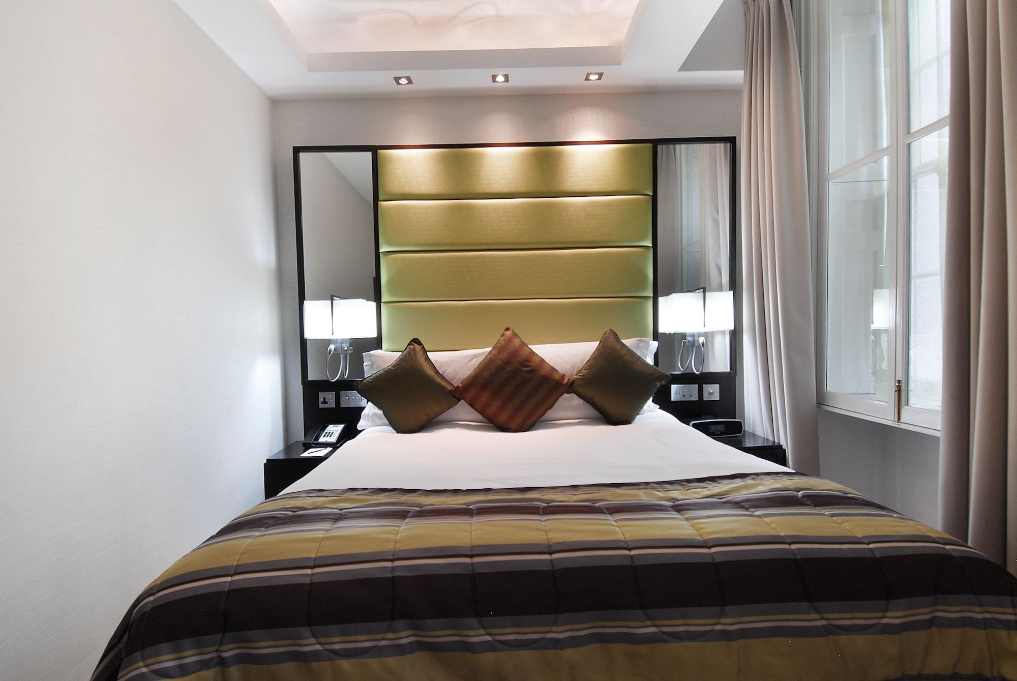 Hotel Montcalm Brewery Townhouse London Exterior foto The photo shows a stylishly decorated bedroom. The bed is centered in the room, featuring a white comforter with a plaid pattern in shades of brown and green. There are three decorative pillows on the bed, two in shades of brown and one in dark green