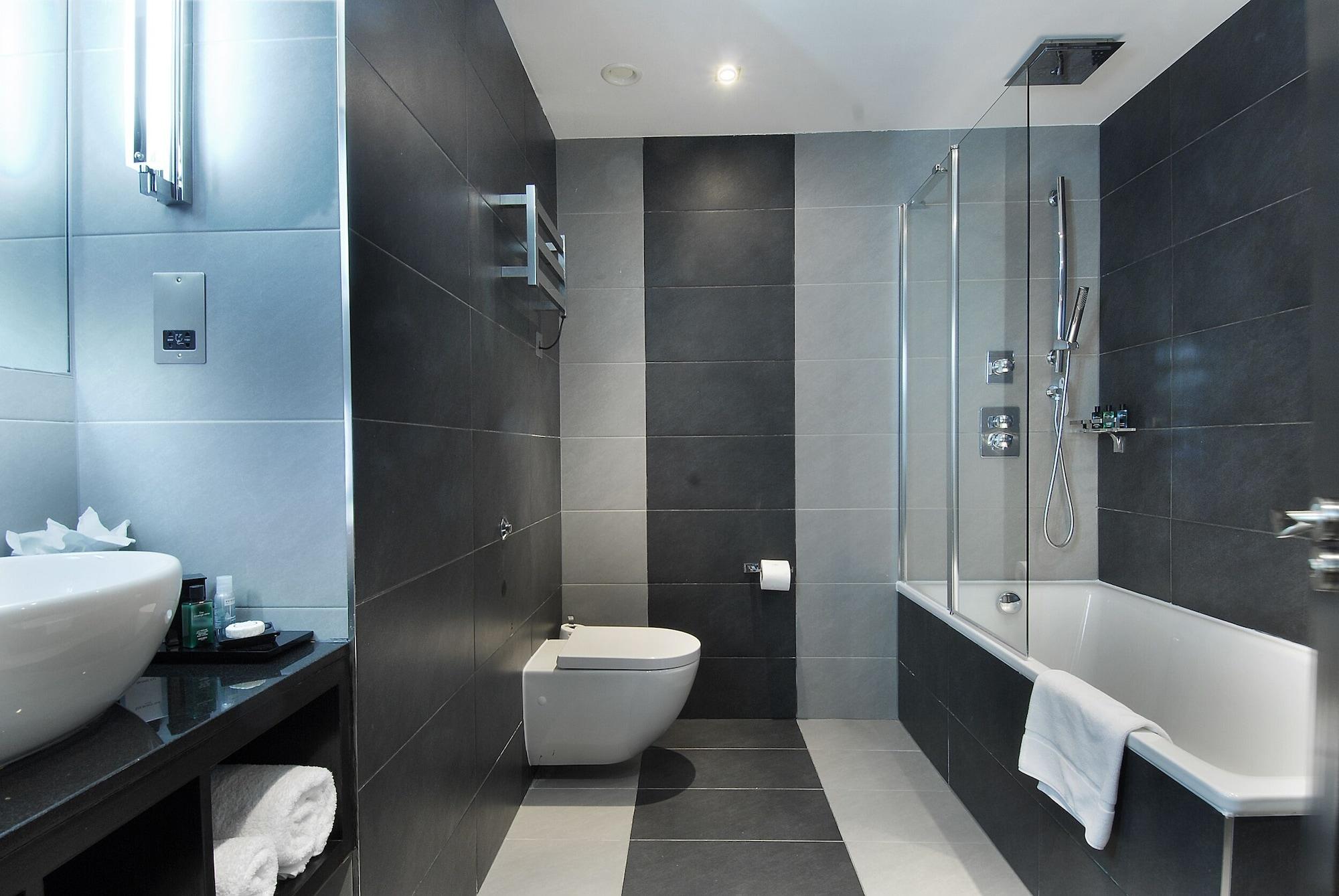 Hotel Montcalm Brewery Townhouse London Exterior foto The photo shows a modern bathroom featuring a sleek design. The walls are tiled in a combination of dark gray and light gray, creating a contemporary look. On the left, there is a countertop with a basin and some toiletries placed on it. The middle s