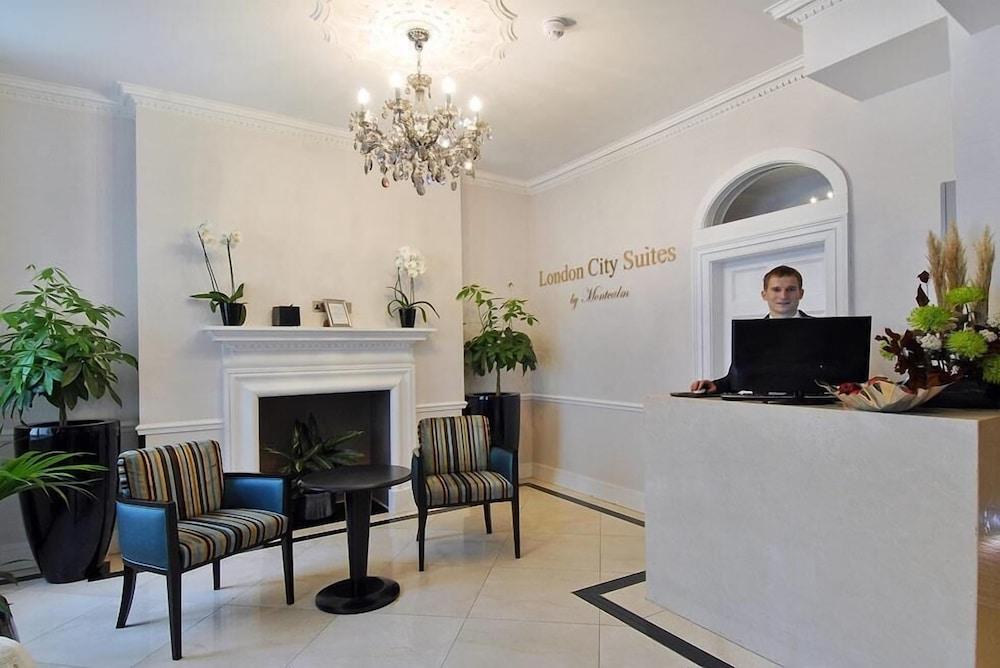 Hotel Montcalm Brewery Townhouse London Exterior foto The photo shows the interior of a reception area in a hotel called "London City Suites." The space features a light-colored wall with the hotel's name displayed. There is a stylish chandelier hanging from the ceiling, providing warm lighting. 

In th
