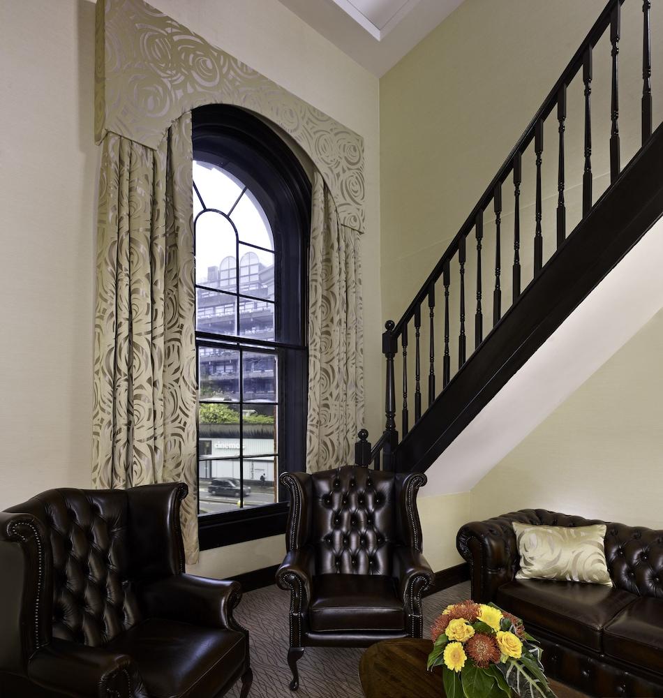 Hotel Montcalm Brewery Townhouse London Exterior foto The photo shows a cozy interior space featuring two elegant leather armchairs placed near a large, ornate window with arched top and decorative curtains. The wall is painted in a muted color, enhancing the warmth of the room. A staircase with black s
