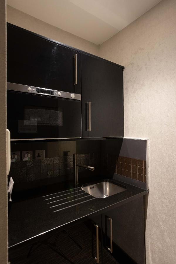 Hotel Montcalm Brewery Townhouse London Exterior foto The photo shows a modern kitchen setup with a dark color scheme. It features:

- A built-in microwave oven situated above a countertop.
- A sleek black cabinet beneath the microwave, which likely stores kitchen items.
- A stainless steel sink placed 