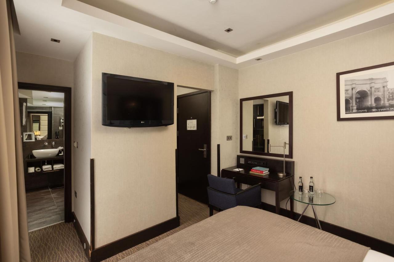 Hotel Montcalm Brewery Townhouse London Exterior foto The photo shows a hotel room featuring a double bed with a neutral-colored bedspread. On one wall, there is a flat-screen TV mounted. Adjacent to the bed, there is a stylish desk with a chair and a small glass table. A mirror is positioned above the 
