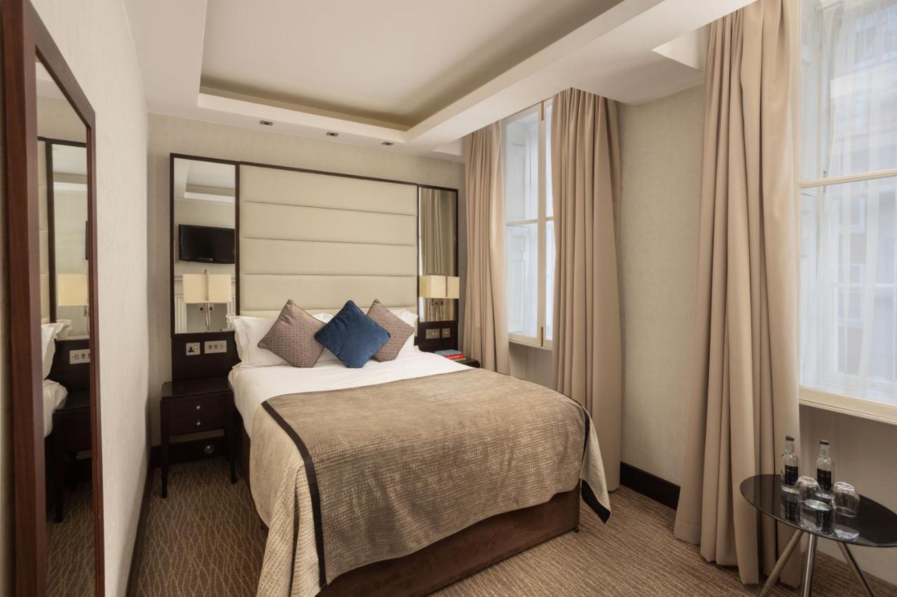 Hotel Montcalm Brewery Townhouse London Exterior foto The photo shows a cozy hotel bedroom. The room features a neatly made double bed with a beige bedspread and decorative pillows, including a blue one. There are bedside tables on either side of the bed with lamps. The walls are painted in a soft color