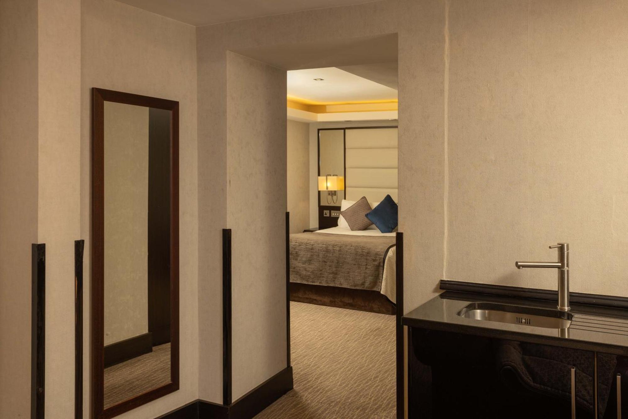 Hotel Montcalm Brewery Townhouse London Exterior foto The photo shows an interior space that appears to be part of a hotel room or suite. There is a doorway leading into a bedroom area, where a bed with decorative pillows is visible. In the foreground, there's a tall mirror on the left side and a small 