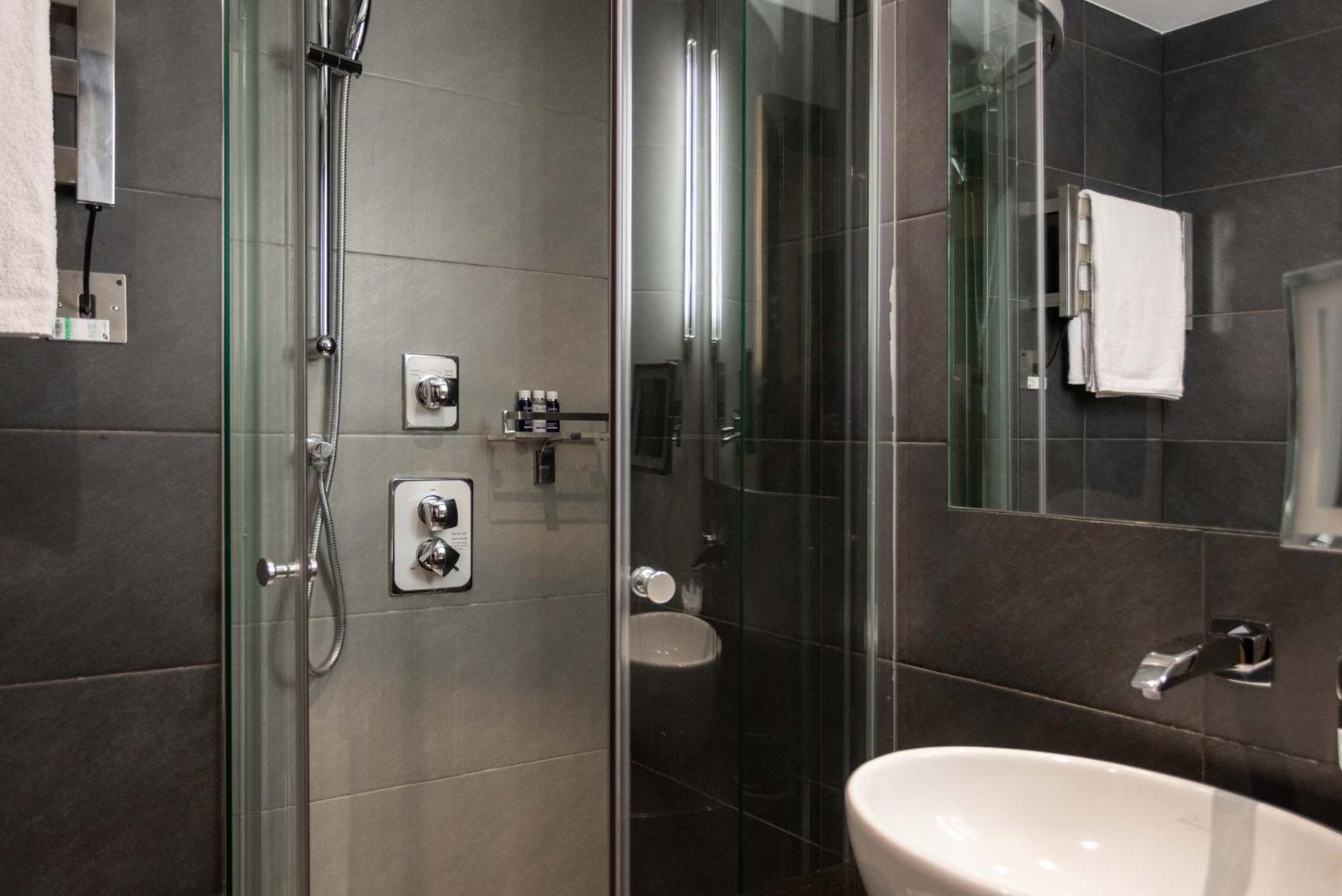 Hotel Montcalm Brewery Townhouse London Exterior foto The photo shows a modern bathroom with a glass shower enclosure. The shower features a handheld showerhead and various controls mounted on the wall. The walls are tiled in dark, sleek tones, contributing to a contemporary aesthetic. There is a round 