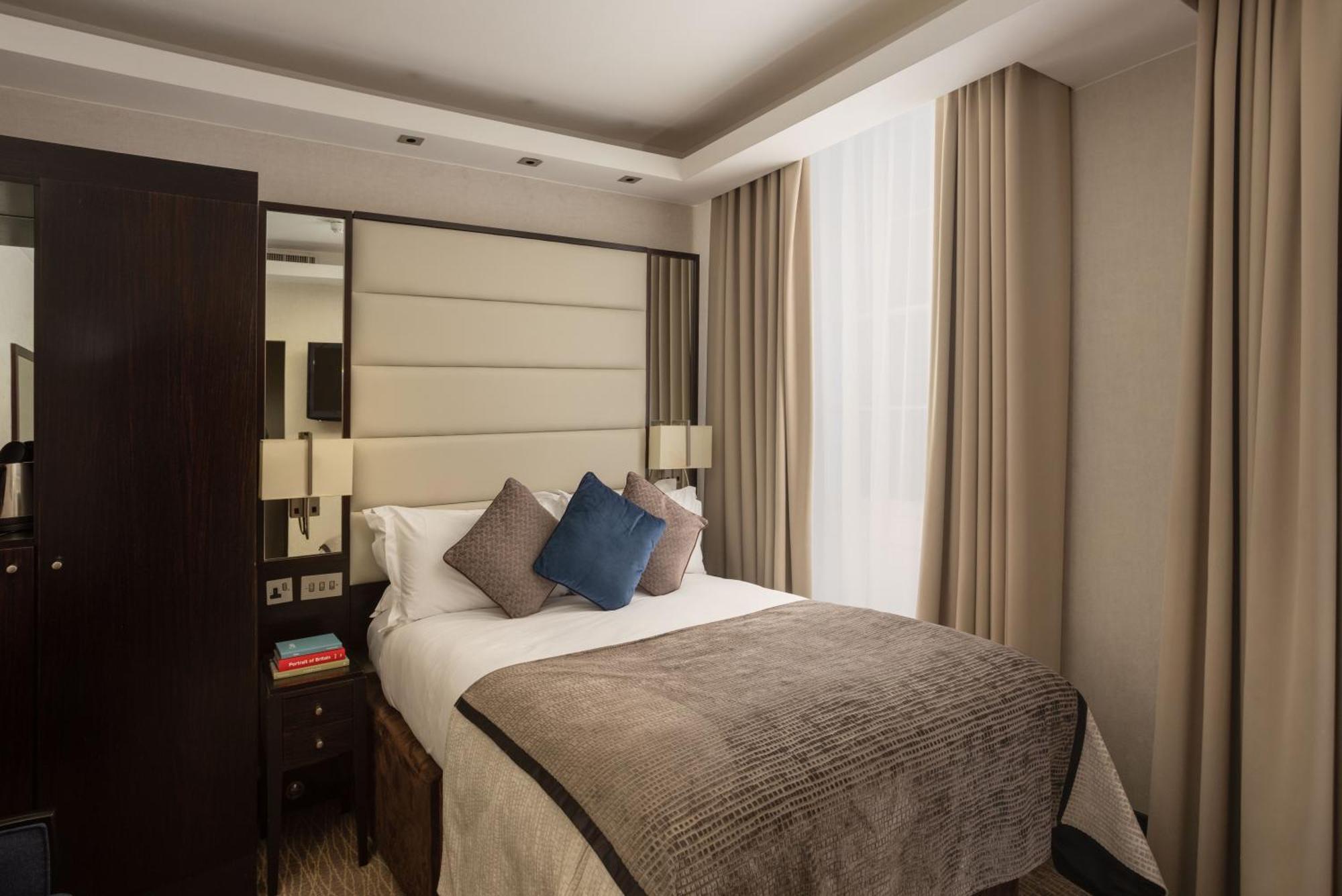 Hotel Montcalm Brewery Townhouse London Exterior foto The photo shows a modern hotel room with a cozy design. It features a double bed with a light-colored headboard and a soft, stylish blanket. There are decorative pillows on the bed, including a blue one. On either side of the bed, there are small nig