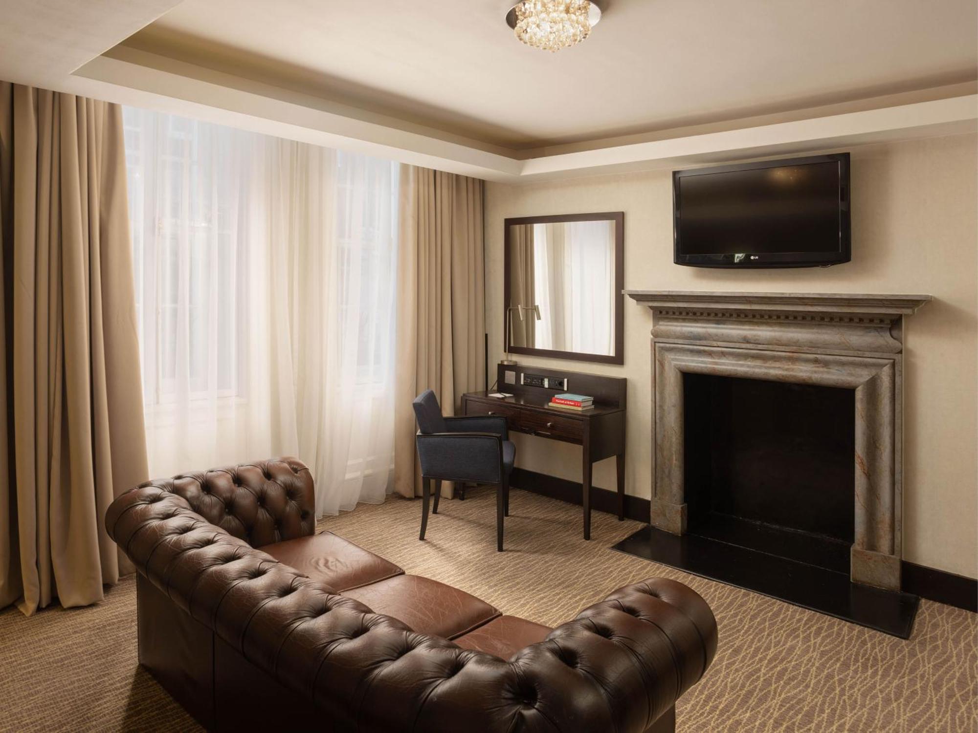 Hotel Montcalm Brewery Townhouse London Exterior foto The photo shows a cozy and elegantly designed room. There is a comfortable brown leather sofa with tufted detailing. A small desk and chair are positioned near a mirror, providing a space for work or personal grooming. On the wall, a flat-screen TV i