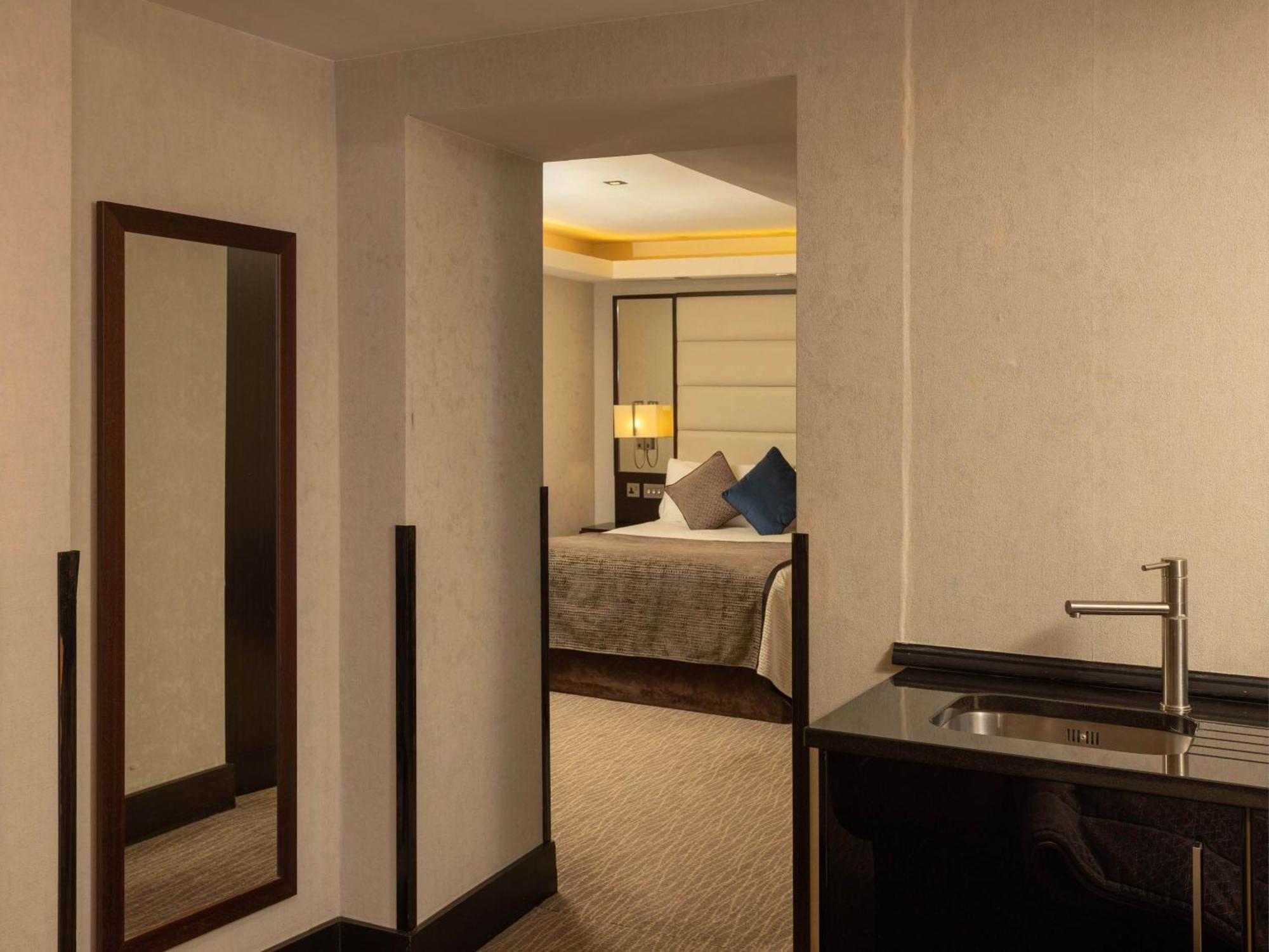 Hotel Montcalm Brewery Townhouse London Exterior foto The photo shows an interior space that appears to be a hotel room or a suite. There is a doorway leading to a bedroom visible in the background, where a bed with decorative pillows can be seen. To the side, there is a small wet bar or kitchenette are