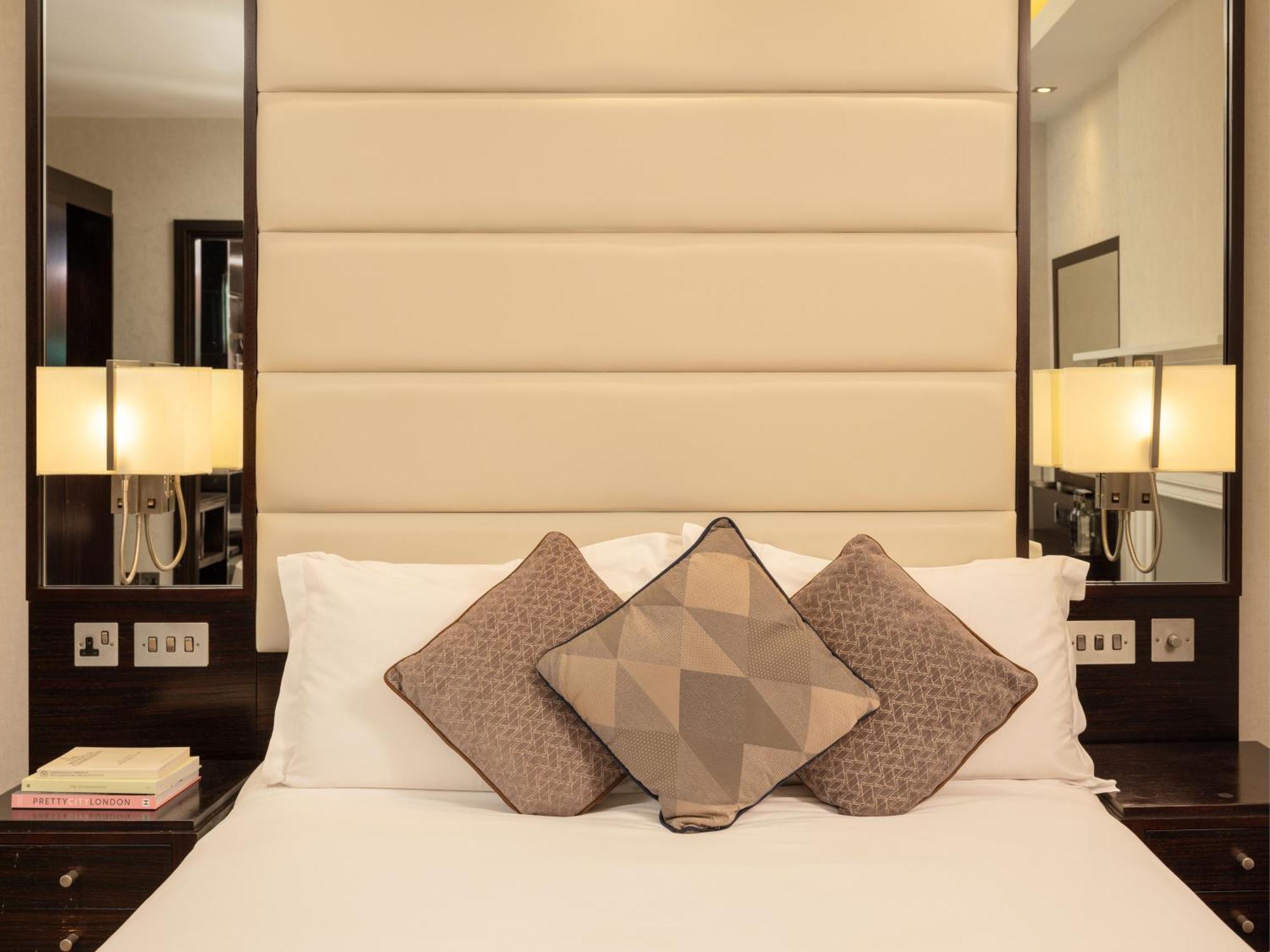 Hotel Montcalm Brewery Townhouse London Exterior foto The image shows a cozy bedroom setting. The bed features a headboard upholstered in a light beige fabric. It is adorned with three decorative pillows in varying patterns and colors, placed on white bedding. On either side of the bed, there are modern