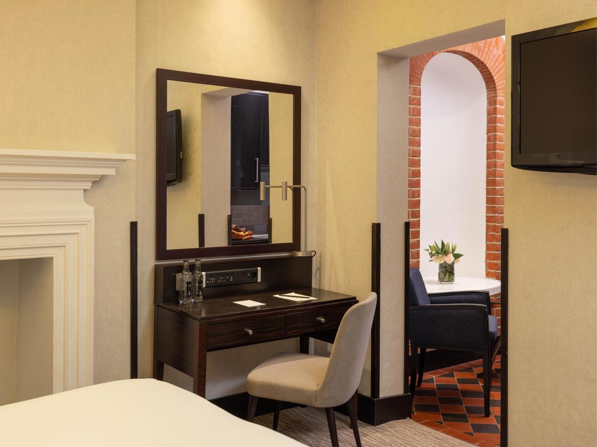Hotel Montcalm Brewery Townhouse London Exterior foto The photo displays a hotel room setup. On the left side, there's a bed with a simple white bedding arrangement. Adjacent to the bed, there's a wooden desk with a chair, along with a mirror above the desk. The desk area is equipped with some glassware