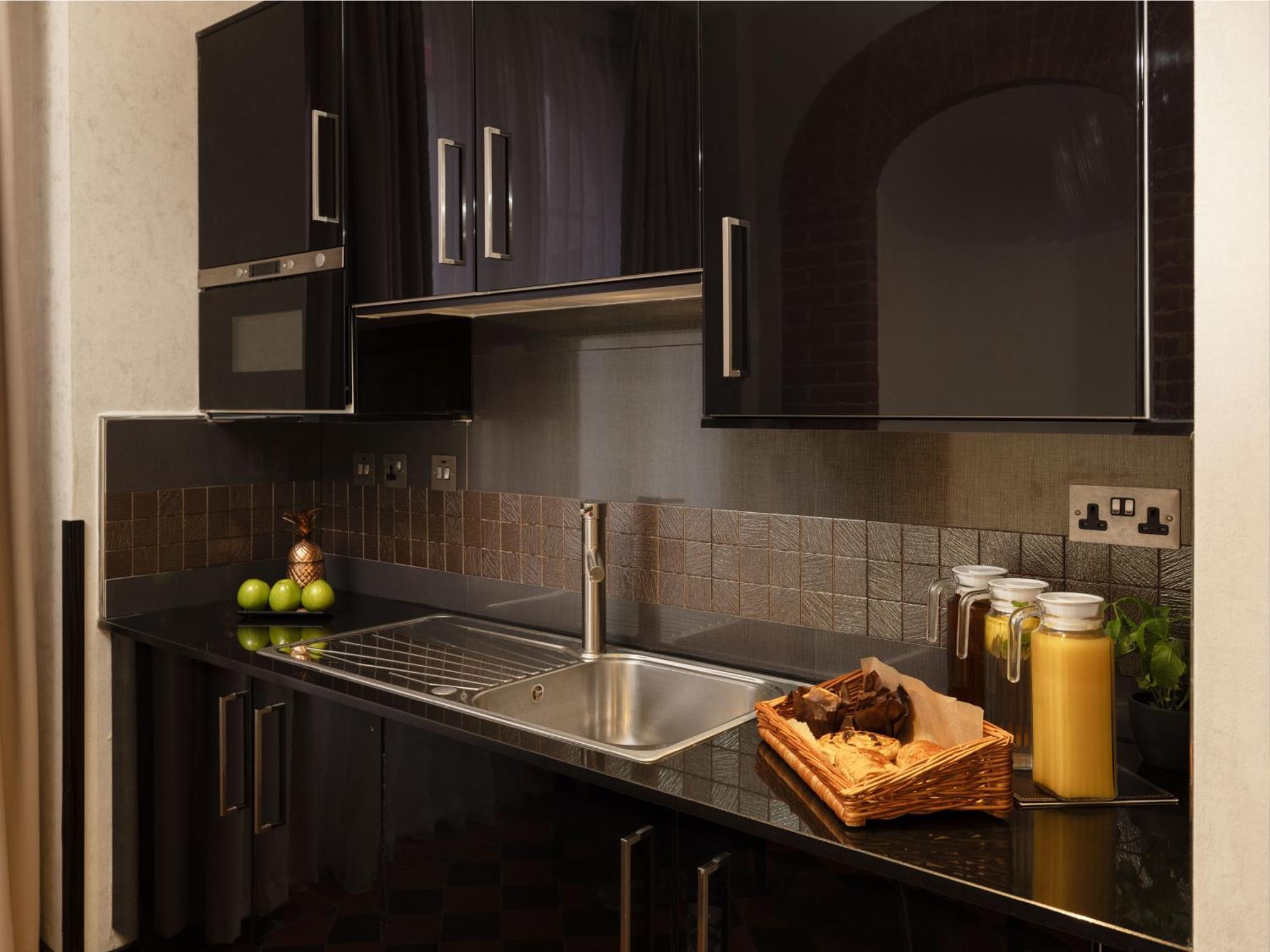 Hotel Montcalm Brewery Townhouse London Exterior foto The photo shows a modern kitchen with sleek black cabinetry and a glossy finish. The kitchen features a stainless steel sink with a contemporary faucet, set against a dark, textured countertop. Above the counter, there are cabinets that match the cou
