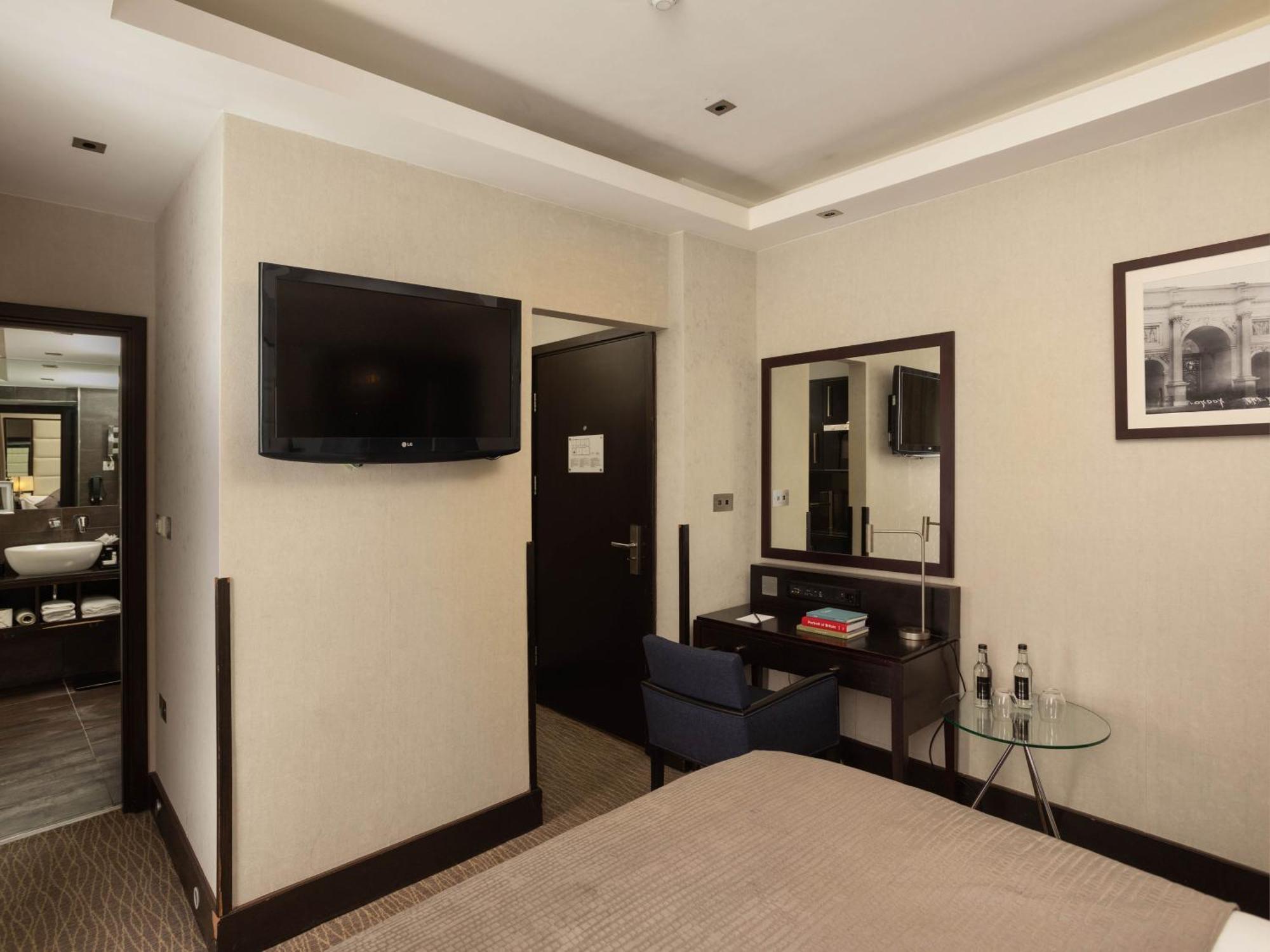 Hotel Montcalm Brewery Townhouse London Exterior foto The photo shows a hotel room with a modern and minimalist design. On the left, there's a wall-mounted flat-screen TV. In the center, there's a bed with a neutral-colored bedspread. To the right of the bed, there is a small desk with a mirror above it
