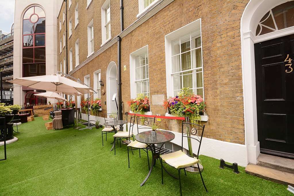 Hotel Montcalm Brewery Townhouse London Exterior foto The photo depicts a charming outdoor area in front of a building with a warm, textured brick facade. There is a neatly maintained lawn, likely made of artificial grass, and several small round tables with chairs are arranged outside. Flower pots with
