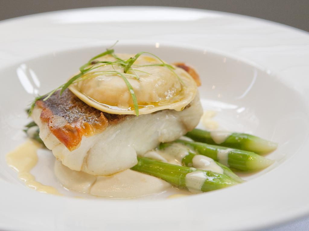 Hotel Montcalm Brewery Townhouse London Exterior foto The image shows a beautifully presented dish featuring a piece of fish, likely a white fish, topped with a clam. It is served on a bed of green asparagus spears. The dish is garnished with thinly sliced herbs or greens, adding a touch of color. The s