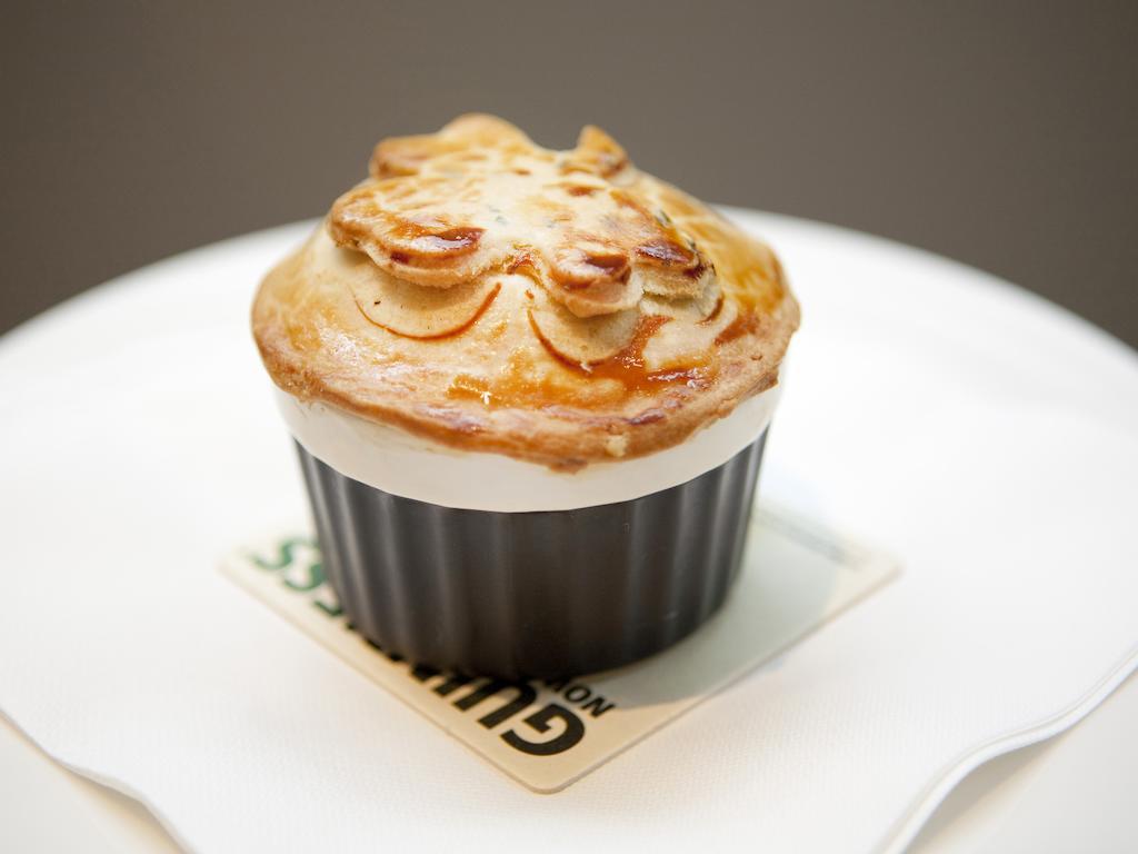 Hotel Montcalm Brewery Townhouse London Exterior foto The photo shows a small, individual serving of a pie, likely a savory dish. It has a golden-brown crust with decorative elements on top, resembling leaves or floral patterns. The pie is served in a black dish and placed on a white plate. The overall 