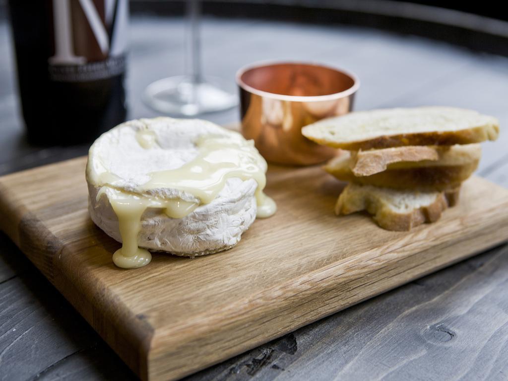 Hotel Montcalm Brewery Townhouse London Exterior foto The photo features a wooden serving board with several items. There is a round cheese, likely Brie or a similar soft cheese, that appears to be melting and dripping slightly. Next to the cheese, there is a small copper cup that might contain a sauce 