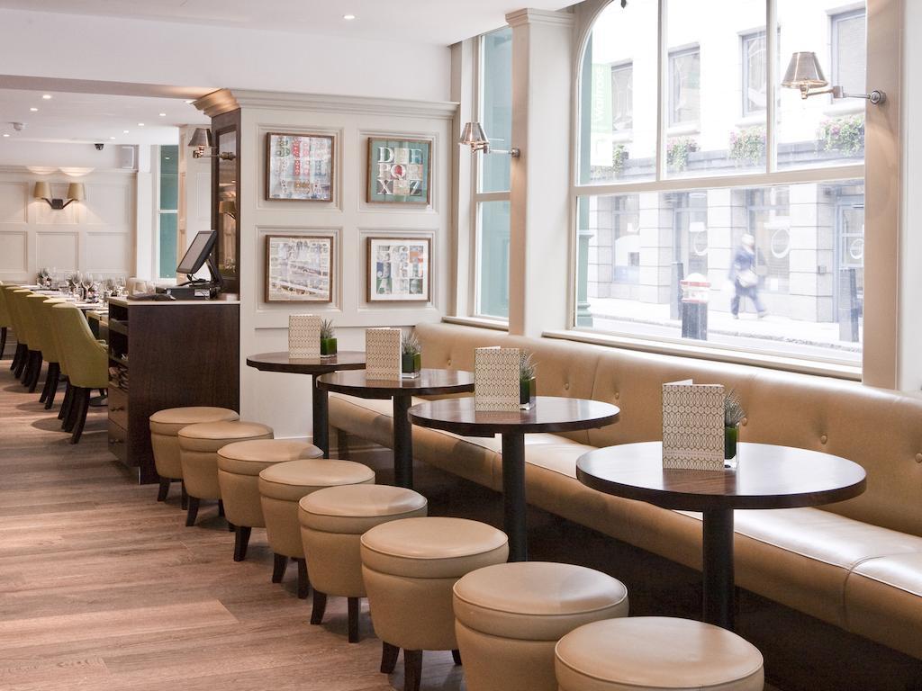 Hotel Montcalm Brewery Townhouse London Exterior foto The photo displays a modern café or restaurant interior. There is a cozy seating area featuring light-colored, upholstered benches along the wall, accompanied by small round tables. The tables are paired with circular stools. The decor includes frame