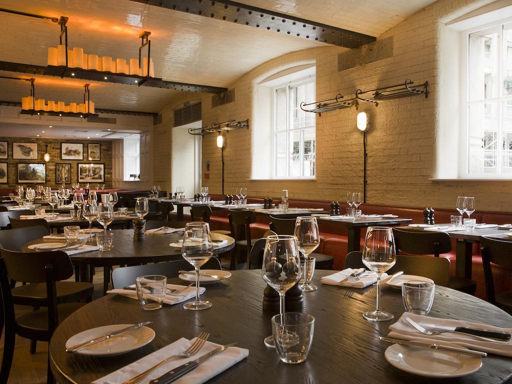 Hotel Montcalm Brewery Townhouse London Exterior foto The photo shows a restaurant interior featuring a warm and inviting atmosphere. It has several round wooden tables set for dining, each with neatly arranged plates, utensils, and glasses. The lighting is soft, with overhead fixtures providing a cozy 