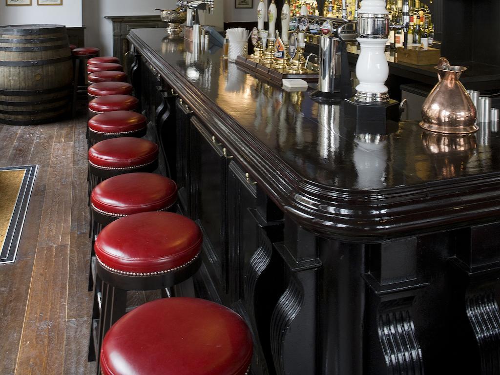 Hotel Montcalm Brewery Townhouse London Exterior foto The photo shows a bar setting with a long, polished dark wooden bar counter. Attached to the counter are several bar stools with red leather seats. Behind the bar, there are various bottles, suggesting a well-stocked bar. The flooring appears to be w