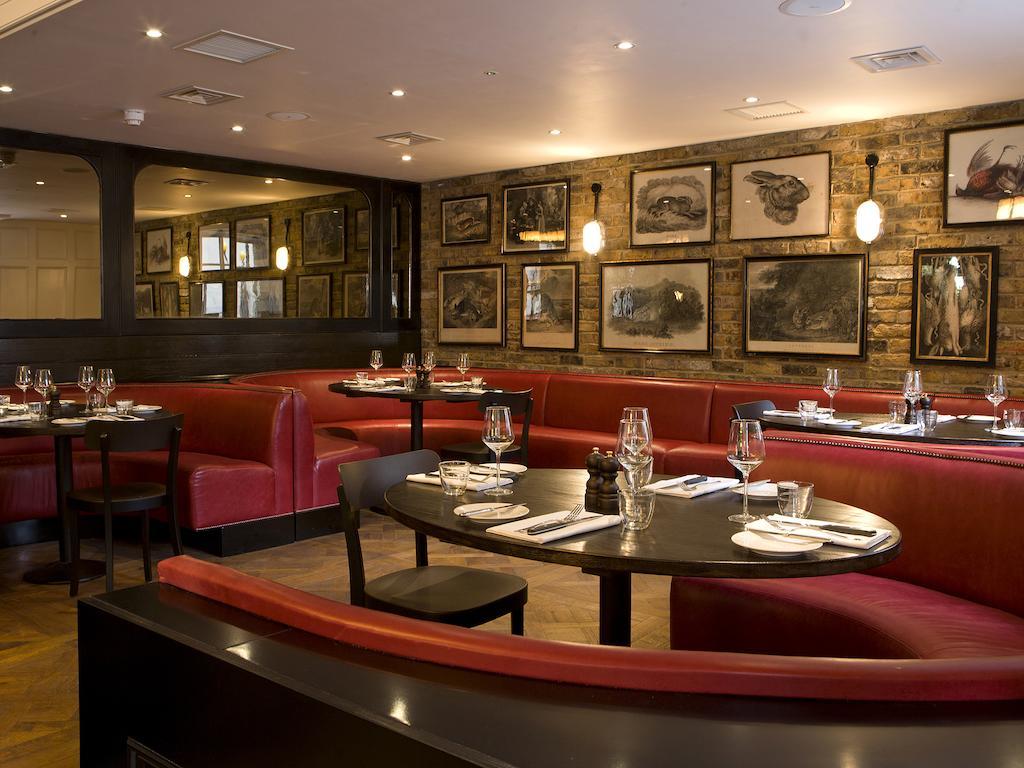 Hotel Montcalm Brewery Townhouse London Exterior foto The photo depicts an elegant restaurant interior. There are curved red booths along the walls, creating a cozy seating arrangement. The tables are round and set with white plates and glassware, indicating a prepared dining area. The walls feature a n