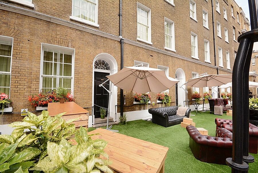 Hotel Montcalm Brewery Townhouse London Exterior foto The photo depicts an outdoor area of a building with a brick facade. There are several large windows visible, along with a wooden door. The setting features outdoor furniture, including couches in a dark leather finish and wooden tables. Large umbrel